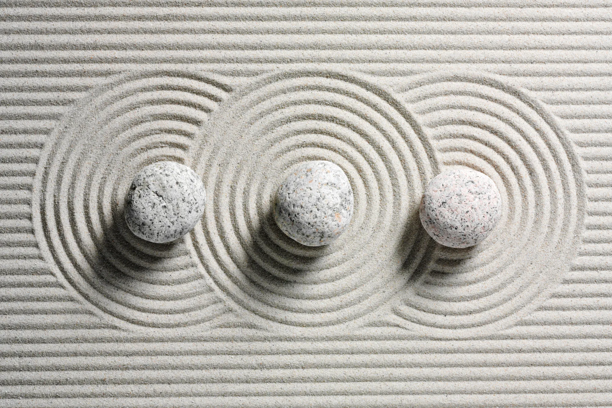 Zen garden with three round stones and concentric circles raked in fine sand, symbolizing wellness and balance.