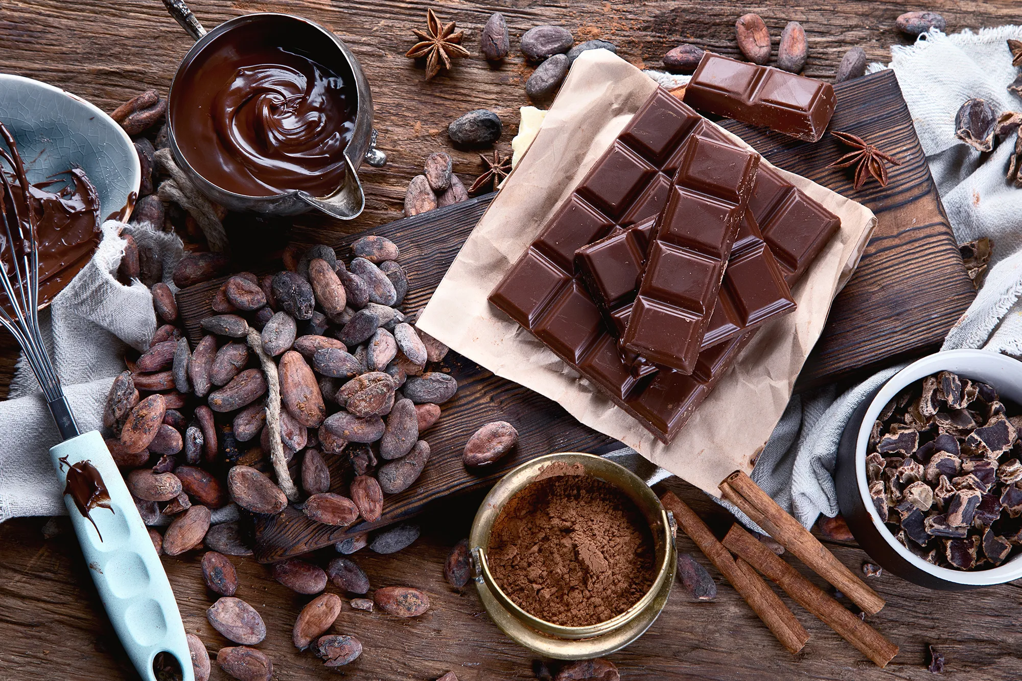 Flat lay of chocolate bars, cocoa beans, and spices on a rustic wooden table, representing gourmet chocolate.