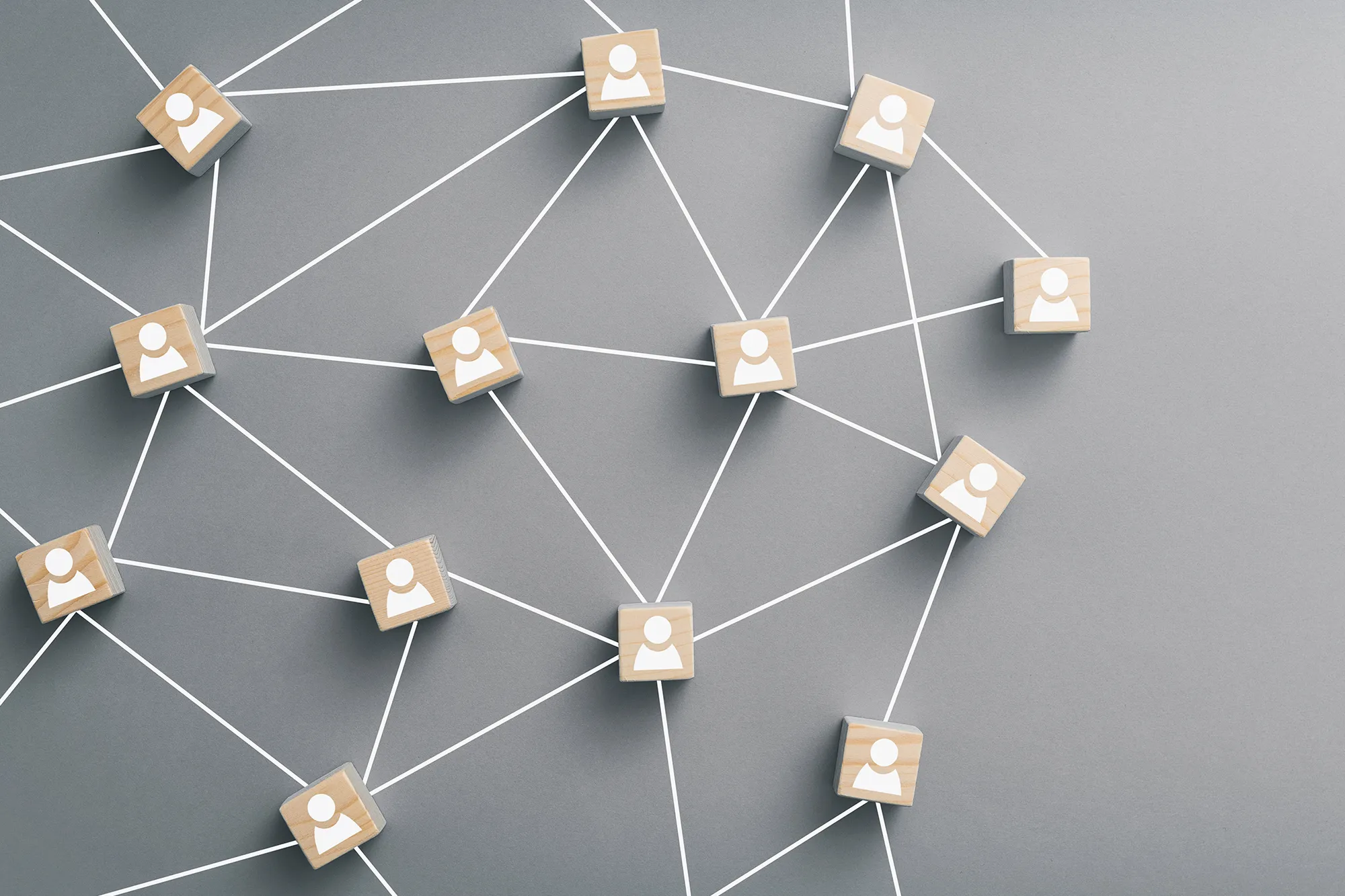 Wooden cubes with human icons connected by white lines on a gray surface, symbolizing networking, communication, and business connections.