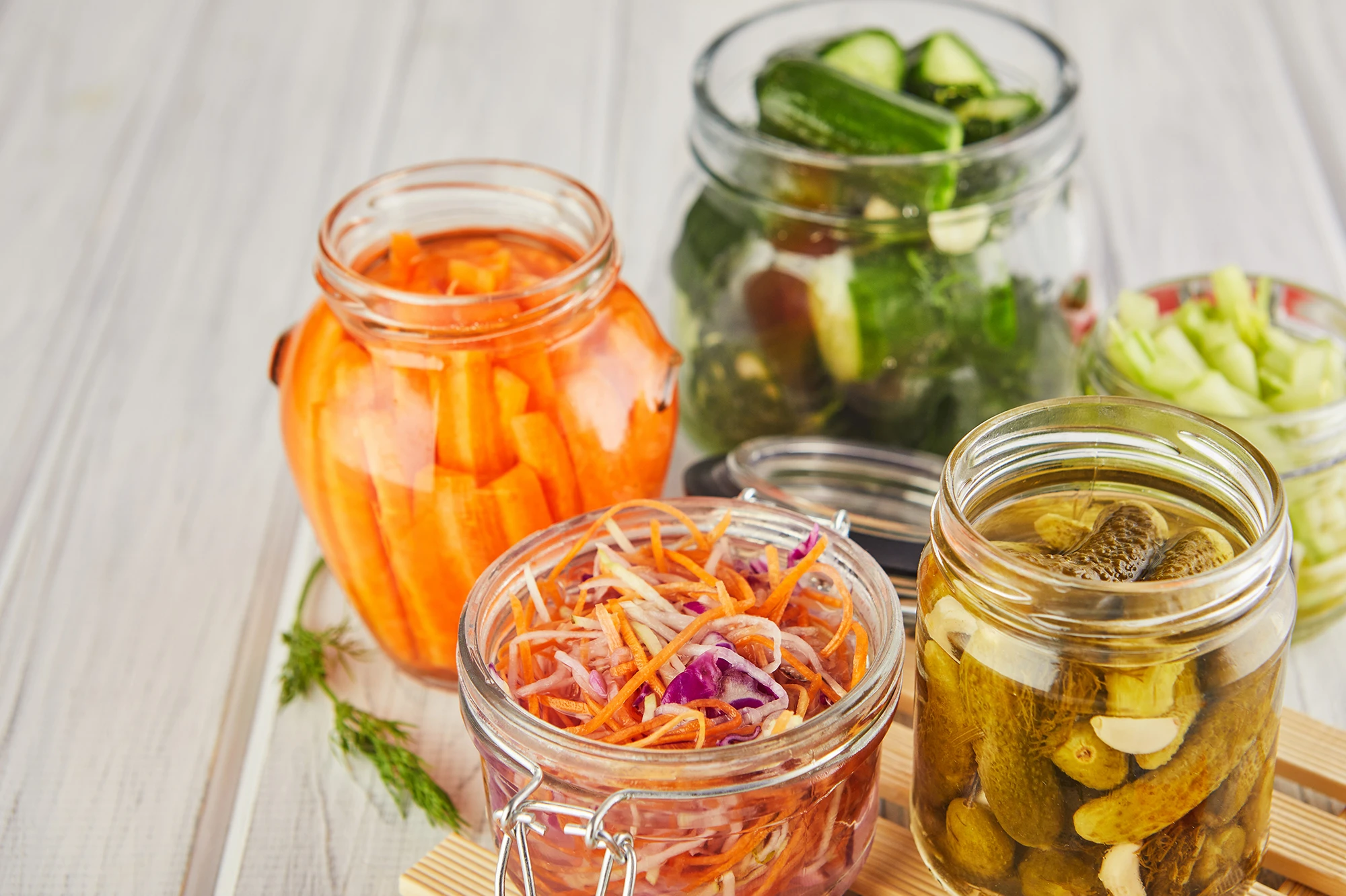 Glass jars filled with pickled cucumbers, carrots and shredded vegetables on a wooden table.