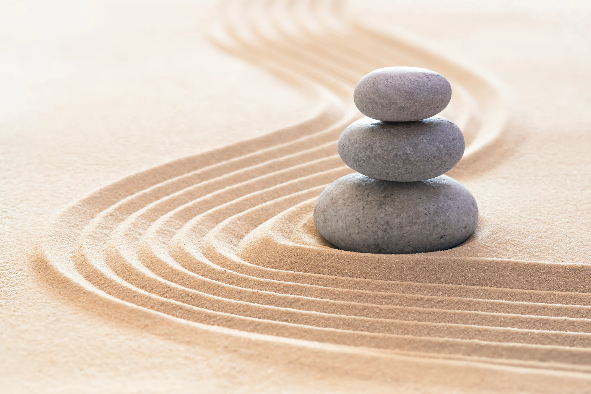 Three smooth stones stacked beside curved lines raked into pale sand.